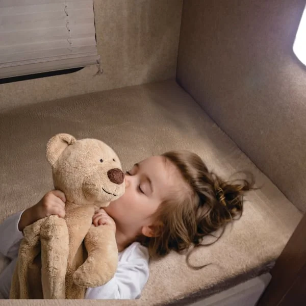 Child kisses teddy bear on RV bed
