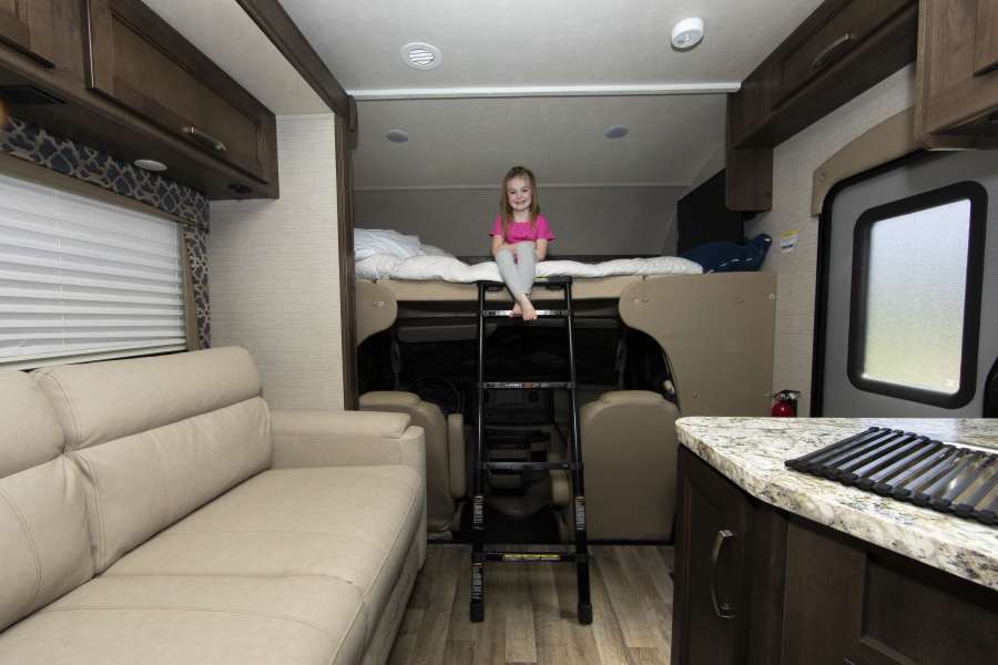 Child sitting on a bed in an RV with an RV sofa and other appliances